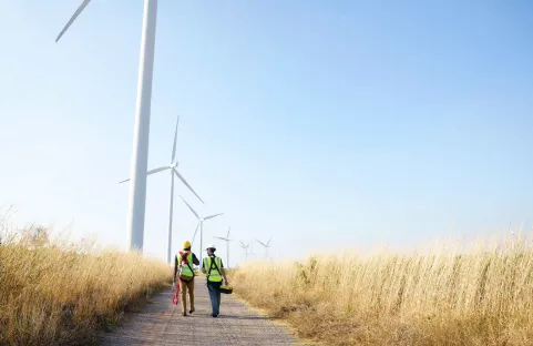 Dois trabalhadores especializados em frente a aerogeradores terrestres num campo de trigo